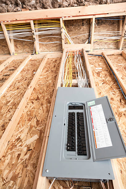 Electrical breaker panel with open cover installed on plywood floor, showing multiple wires running to wall framing in an unfinished building interior—ideal for future panel upgrades.